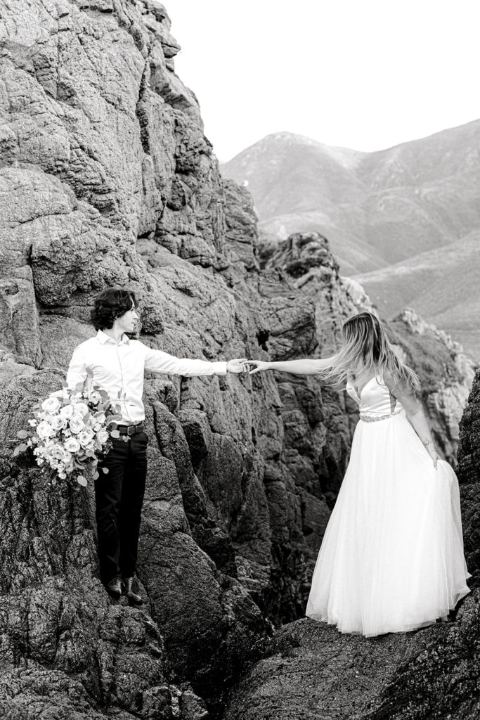 Black and white Big Sur elopement photo of the couple holding hands over the cliffs