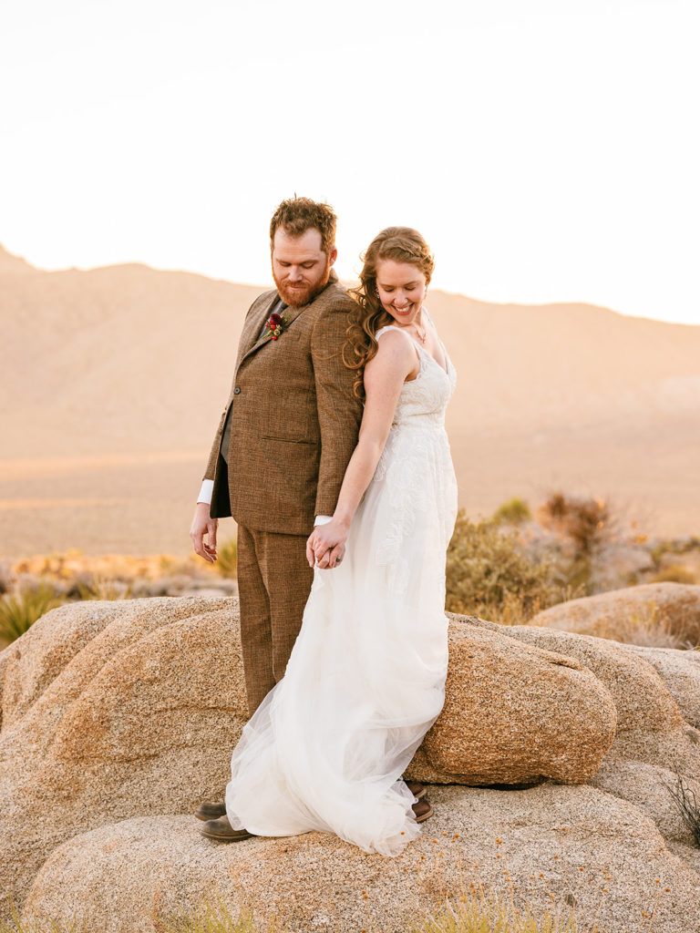 Couple stands back to back, holding hands at Joshua Tree